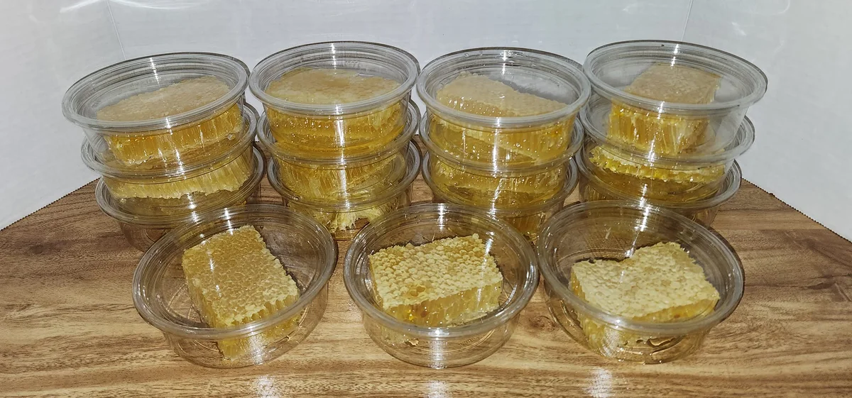Golden pieces of capped honeycomb portioned into clear containers on a wooden surface