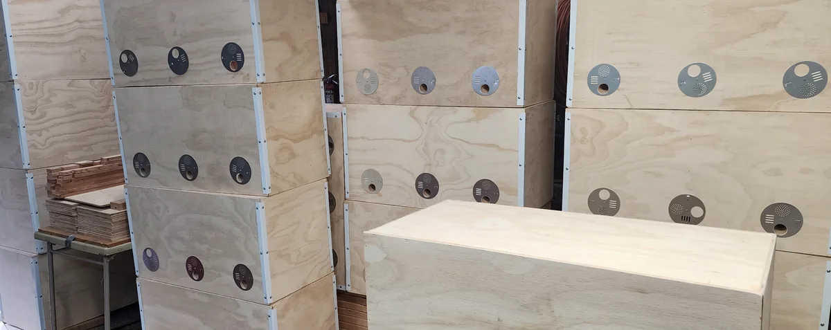 Rows of wooden Generational Hive bodies showing their circular entrance discs and metal corner trim