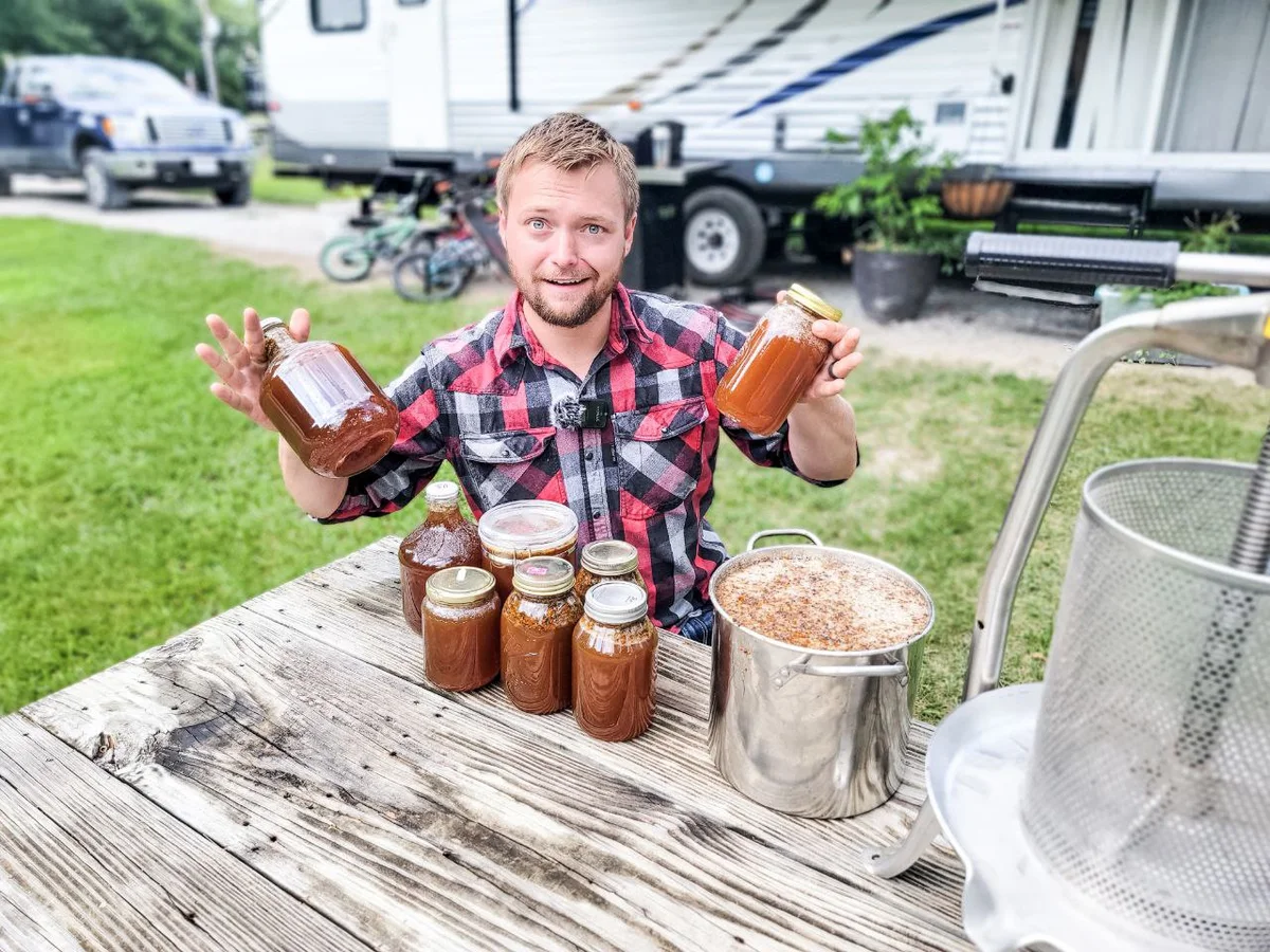 Jamon Mysliwiec holding two jars of honey beside a honey extractor and more jars from a harvest
