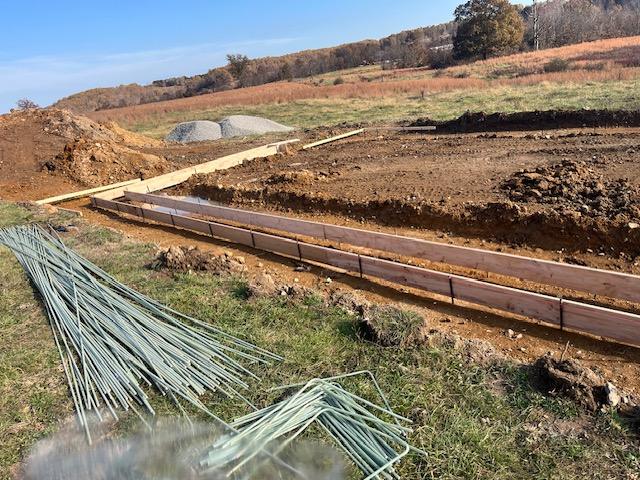 Excavated footing trenches with steel forms and bundles of rebar and green PEX tubing stacked alongside.