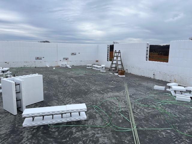 Poured slab with radiant tubing loops visible, surrounded by low ICF wall courses and stacks of foam blocks.