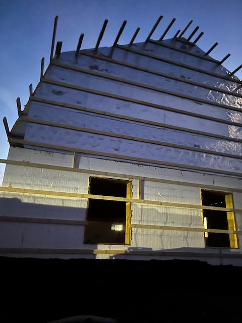 Gable end wall of ICF with vertical rebar projecting from the top of the forms against a blue sky.