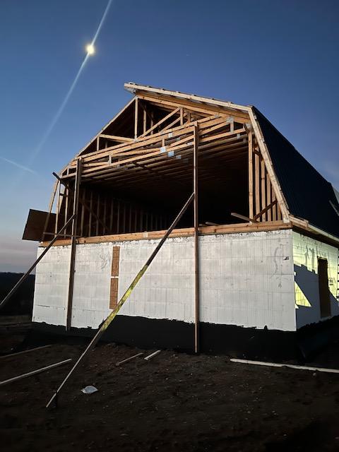 Framed gambrel roof structure sitting on completed ICF walls at dusk.