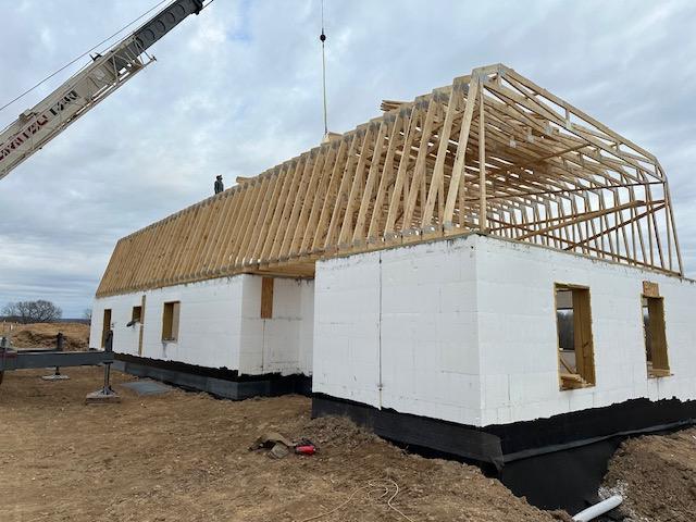 A crane setting wooden roof trusses onto the completed white ICF walls.