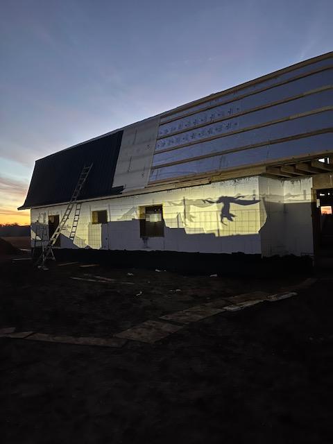 Roof half covered in dark panels and half in exposed insulation board at sunset.