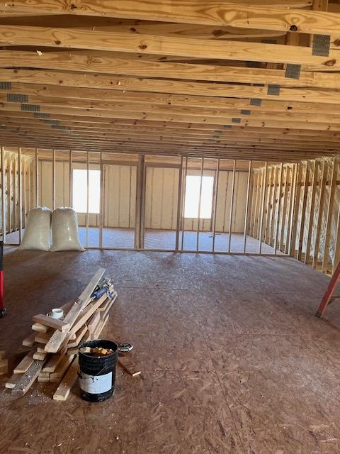 Large open upstairs room with exposed trusses and plywood floor.