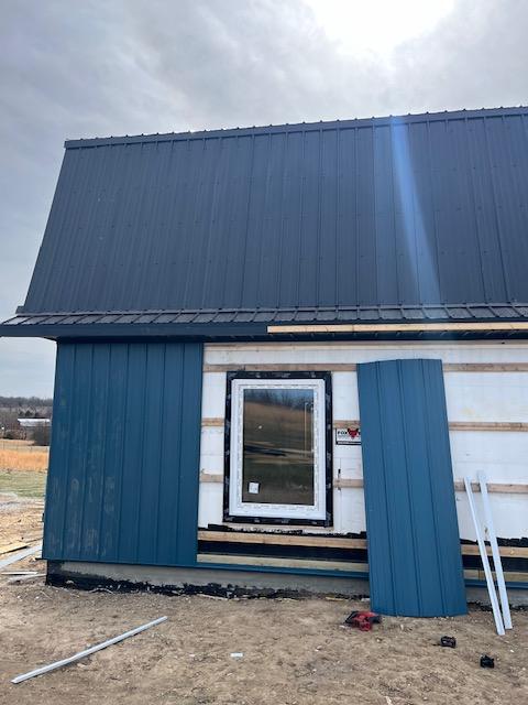 Petrol-blue standing-seam steel siding being installed over exposed insulation board.