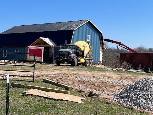 The finished house: a two-story gambrel-roofed barndominium clad in petrol-blue standing-seam steel with a covered entry porch.
